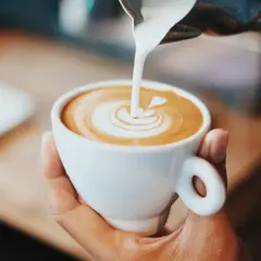 En hand håller en vit kopp med eritreansk kaffe, där mjölk hälls i för att skapa lattekonst.