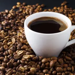 En vit kopp med mörkt, ångande kaffe omgiven av grovmalet kaffe. En perfekt start på dagen.