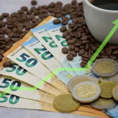 Kaffebönor, eurosedlar och mynt med en grön uppåtgående pil. Det dyra kaffet stiger i pris.