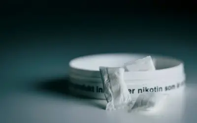 En dosa snus, ett populärt naswar i Sverige, med några påsar framför.
