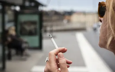 En kvinna röker en cigarett vid en busshållplats. Bilden kan illustrera prisutveckling cigaretter.
