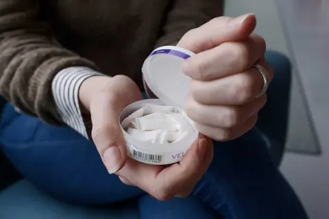 Händer som håller en dosa snus. En kvinna tar fram en prilla ur dosan.