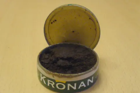 En öppen snusdosa med snus. Kronan-loggan syns tydligt. En klassisk snusdosa storlek.