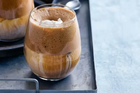 En glas med grekisk frappe, fylld med is och toppad med grädde.