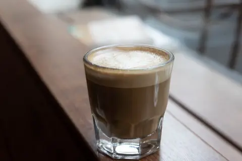 En perfekt cortado macchiato med krämigt skum, serverad i ett glas på en träyta.