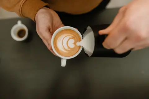 Barista häller mjölkskum i en kopp kaffe för att skapa lattekonst. Vad betyder latte? En kaffedryck med espresso och ångad mjölk.