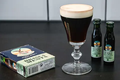 En elegant kaffedrink med krämig topping, bredvid en ask och två små flaskor Branca Menta.