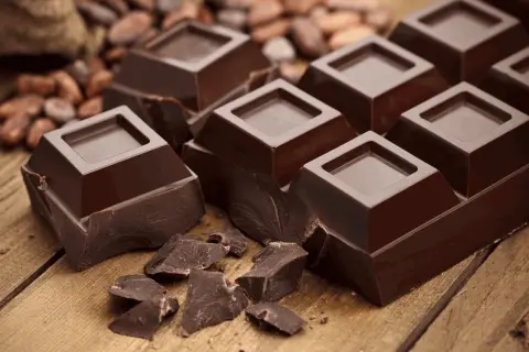 Mörk chokladbitar på träbord, med kakaobönor i bakgrunden. En härlig källa till kakao och koffein för en energikick.