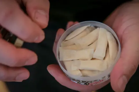 En hand håller en dosa med flera påsar. Det ser ut som fake snus, men det är svårt att säga säkert.