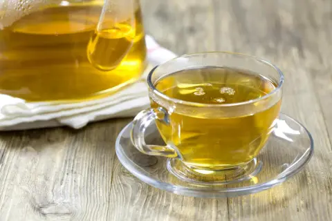 En kopp gyllene kamomillte, utan koffein, står på ett fat bredvid en tekanna.