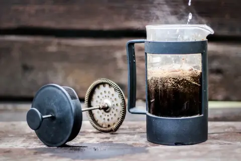 Varmt vatten hälls över kaffepulver i en presskaffe i kaffebryggare. Ånga stiger från den nybryggda drycken.