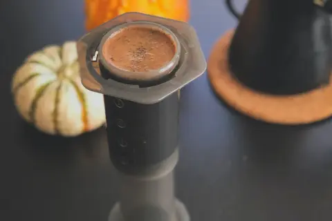En kopp aeropress kaffe med en pumpa i bakgrunden.