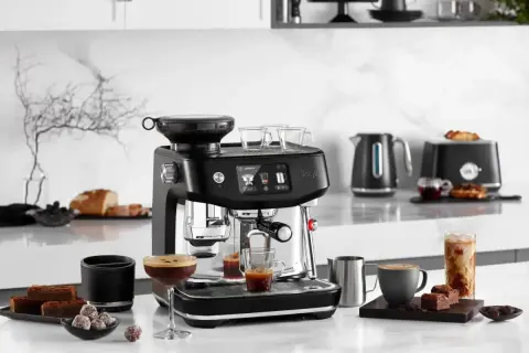 Snygg espressomaskin med inbyggd kvarn, som förbereder vanligt kaffe. Bredvid står godsaker och en kaffekopp.