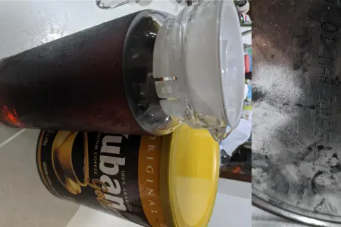 En stor glasburk med kondens fylld med mörkt, gammalt kaffe står bredvid en gul burk med "ubán Gold" kaffe.
