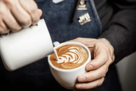 Barista skapar vacker latte art genom att hälla mjölk i en kaffekopp.