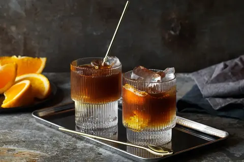 Två glas med kaffe tonic, is och apelsinskivor på ett fat.