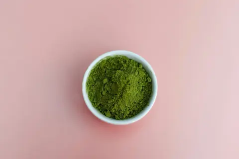 En skål med intensivt grönt matchapulver på en mjukrosa bakgrund. Undrar du vad smakar matcha? Det är en unik, lite bitter och gräsig smak.