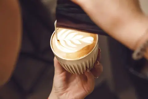 En barista skapar vackert latte art i en kopp kaffe latte.