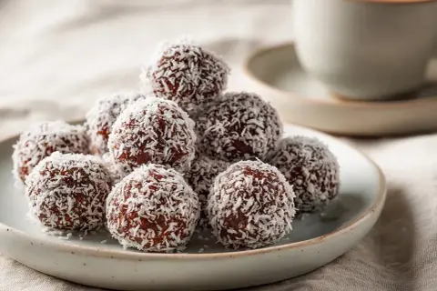 En hög med chokladbollar täckta av kokosflingor, redo att avnjutas med en kopp kaffe.