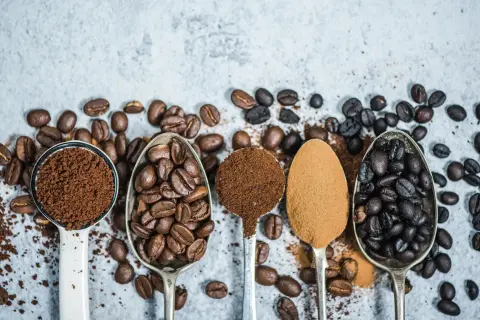 Fem skedar visar olika stadier av kaffe produktion: från hela bönor till fint malet pulver.