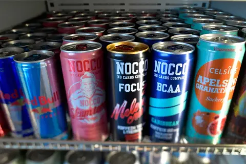 En rad NOCCO-burkar, inklusive "Skumtomte" och "Focus Melon Crush", samt Red Bull och Celsius. Frågan "hur mycket koffein i NOCCO" kan besvaras genom att läsa på burkarna.