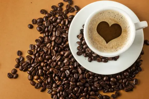 En kopp kaffe med ett hjärta i skummet, omgiven av kaffebönor. En visuell förklaring till hur fungerar koffein.