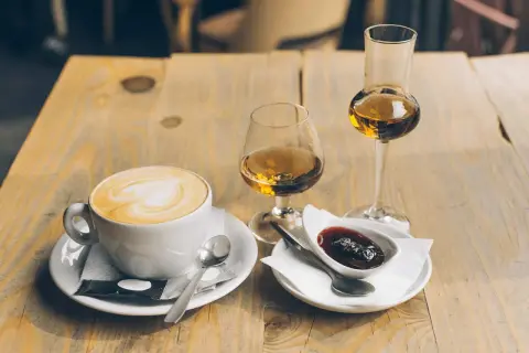 En kopp kaffe med vitt hjärta på skummet, bredvid två glas med bärnstensfärgad dryck och en skål med sylt. En perfekt kombination för en stunds njutning.