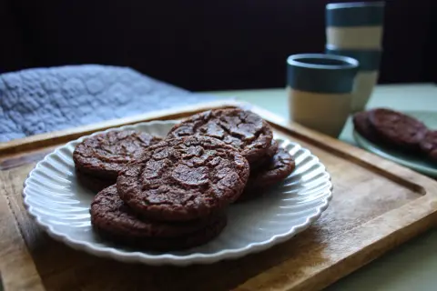 Chokladkakor på en vit tallrik, redo som en snabb kaka till kaffet. Bredvid står staplade muggar.