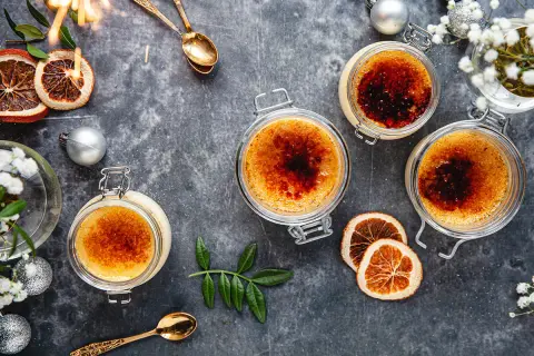 Fyra krämiga creme brulee i glasburkar, toppade med karamelliserat socker. En festlig dukning med torkad apelsin, julgranskulor och gnistrande stjärntändare.