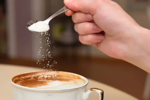 En hand häller socker från en sked ner i en kopp kaffe. Kanske är det salt i kaffet istället för socker?