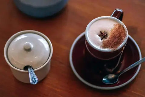 En kopp värmande chai latte med stjärnanis och kanel, bredvid en sockerskål med sked.