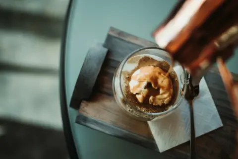 Varm espresso hälls över vaniljglass i en klassisk cafe affogato. En sked ligger bredvid.