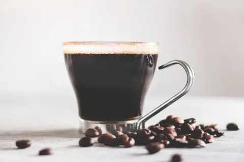 En kopp mörkt kaffe med skum och kaffebönor. Vitt te nyttigt, men en kopp kaffe ger också energi.