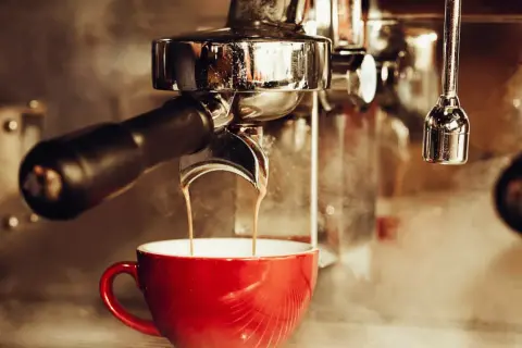 En röd kopp fylls med rykande espresso från en maskin. En klassisk italiensk kaffeupplevelse.