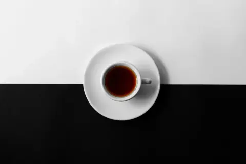 En vit kopp med mörkt kaffe står på en vit tefat, delar en yta som är uppdelad i svart och vitt. Kan kaffe bli gammalt?