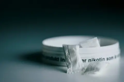 En dosa snus, ett populärt naswar i Sverige, med några påsar framför.