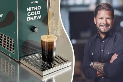 En leende man med tatueringar på armen bredvid en maskin som gör nitro cold brew.