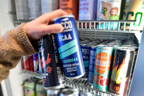 Hand tar en energidryck ur ett kylskåp. Frågan om att dricka energidryck gravid är relevant.