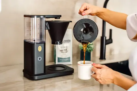 En kaffebryggare som visar hur fungerar en kaffebryggare, med nybryggt kaffe som hälls upp i en mugg.