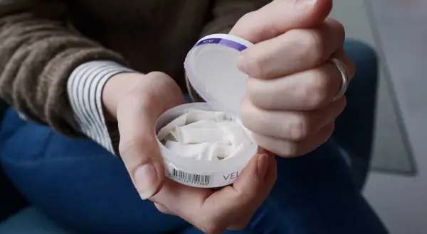 Händer som håller en dosa snus. En kvinna tar fram en prilla ur dosan.