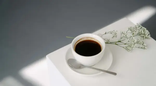 En kopp svart kaffe med en sked och en liten blomsterkvist. Perfekt för en stunds avkoppling med kaffe efter maten.