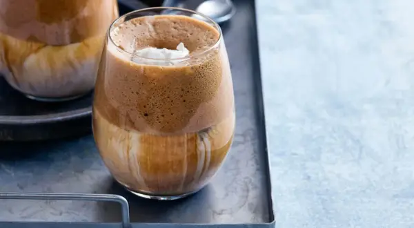 En glas med grekisk frappe, fylld med is och toppad med grädde.