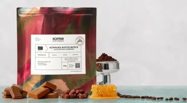 En påse med "Koppars Kaffeinfria Ekologiska Espresso" bredvid choklad, hasselnötter och honungskaka. Perfekt för en liten espresso.