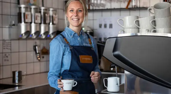 En leende barista håller en kaffekopp. Kanske en påminnelse om hur mycket kaffe dricker svenskar?