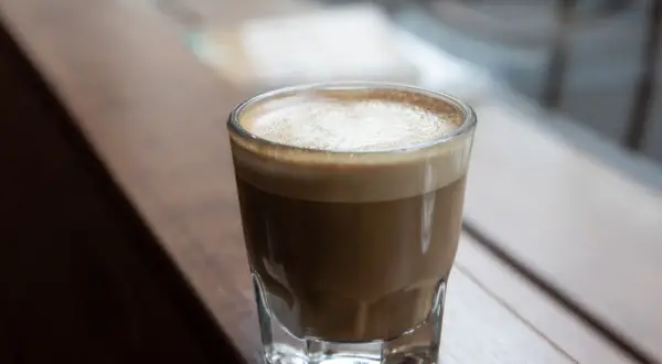 En perfekt cortado macchiato med krämigt skum, serverad i ett glas på en träyta.