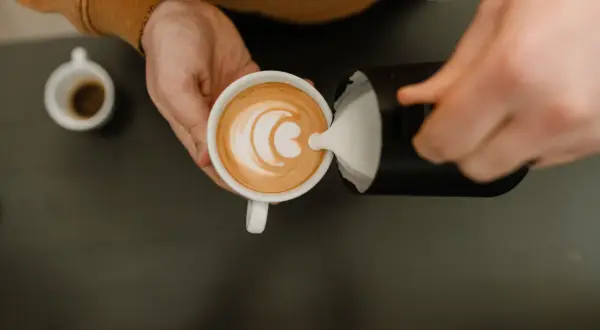 Barista häller mjölkskum i en kopp kaffe för att skapa lattekonst. Vad betyder latte? En kaffedryck med espresso och ångad mjölk.
