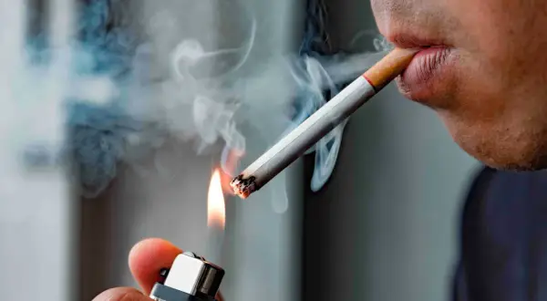 En person tänder en cigarett med en tändare. Röken virvlar upp. Hur mycket nikotin i en cigarett är en viktig fråga för många.