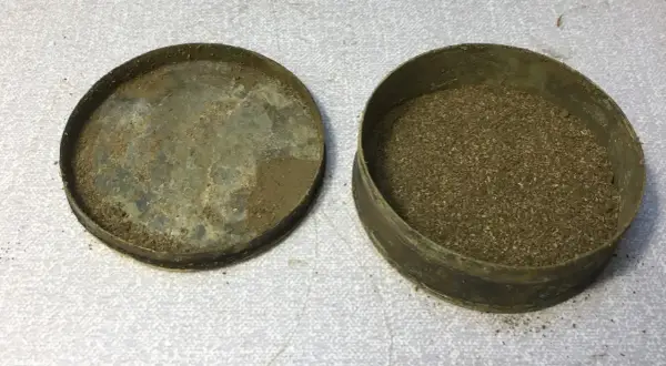 En gammal snusdosa med lock bredvid, fylld med utgånget snus.
