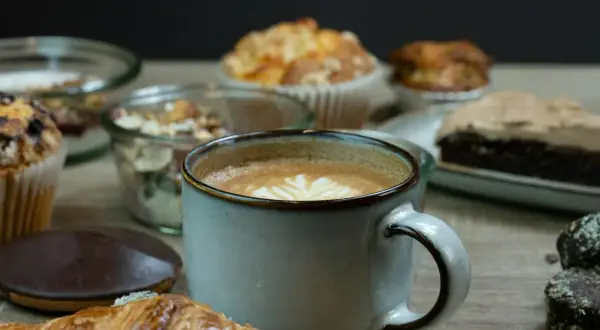 En kopp kaffe med lattekonst, en croissant och olika bakverk. En påminnelse om vart kommer kaffe ifrån och njutningen det ger.