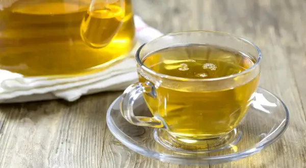 En kopp gyllene kamomillte, utan koffein, står på ett fat bredvid en tekanna.